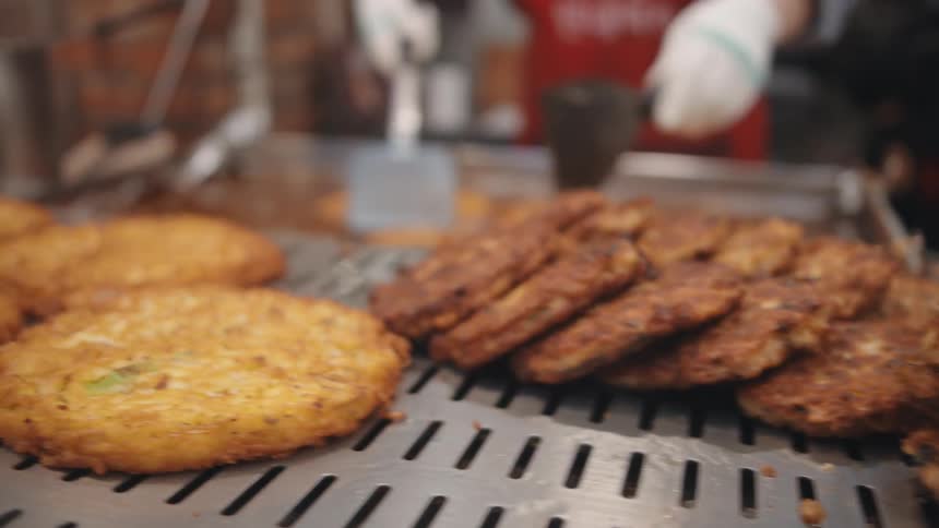 Various meat patties sit on a line in front of a grill