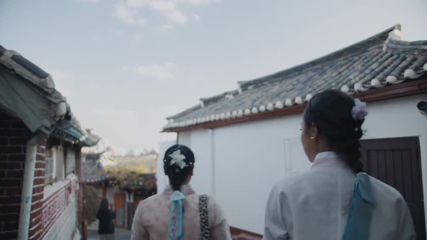 A pair of asian women in traditional clothing following a road between buildings using traditional architecture