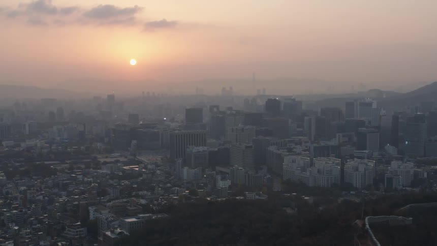 Sun rises over fog shrouded sprawling city bordered by mountains