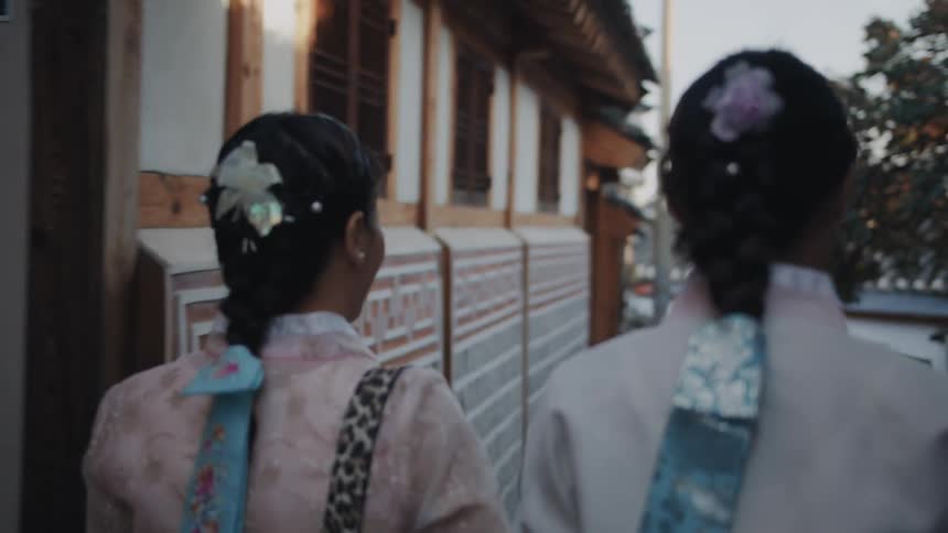 Two women walk between buildings wearing ornate hair ribbons
