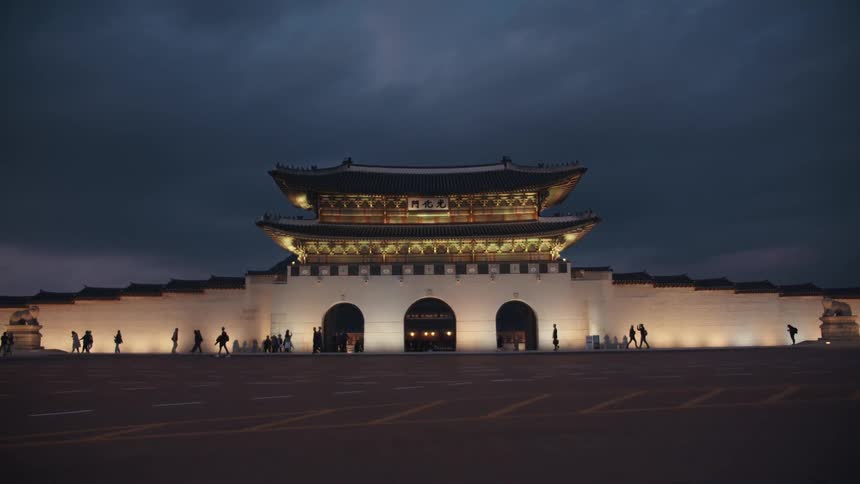 A landmark asian building is illuminated at night as numerous pedestrians pass by it