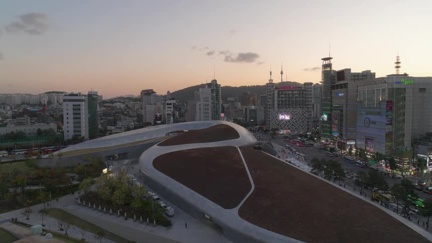 Clouds pass over building with curved roof as traffic and pedestrians move through downtown