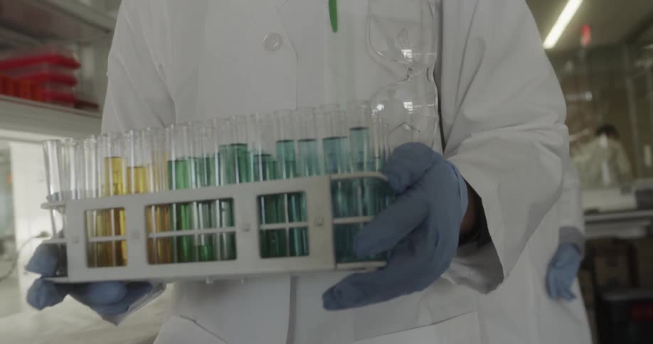 A female scientist carries a tray of test tubes from one microscope to another