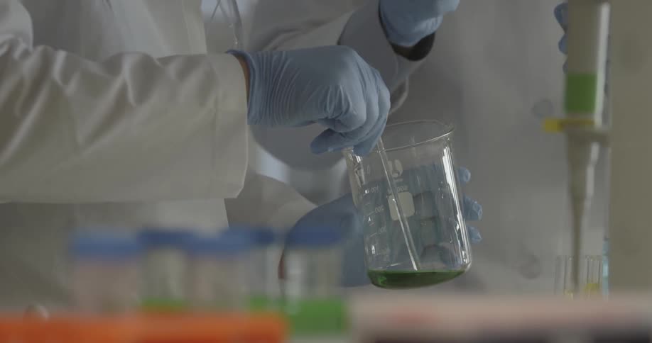 A man stirs a green liquid in a glass beaker