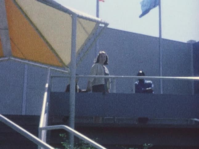 Old footage of a woman holding a boy's hand as they climb a set of stairs at disney world and then turning towards the camera before walking away and waving