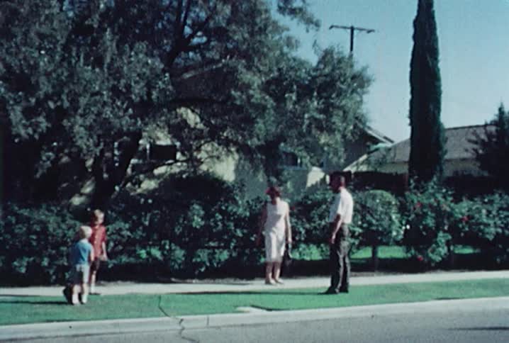 A mother and father turn toward their children on the sidewalk