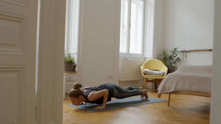 A woman doing yoga on a yoga mat in a bedroom during the day