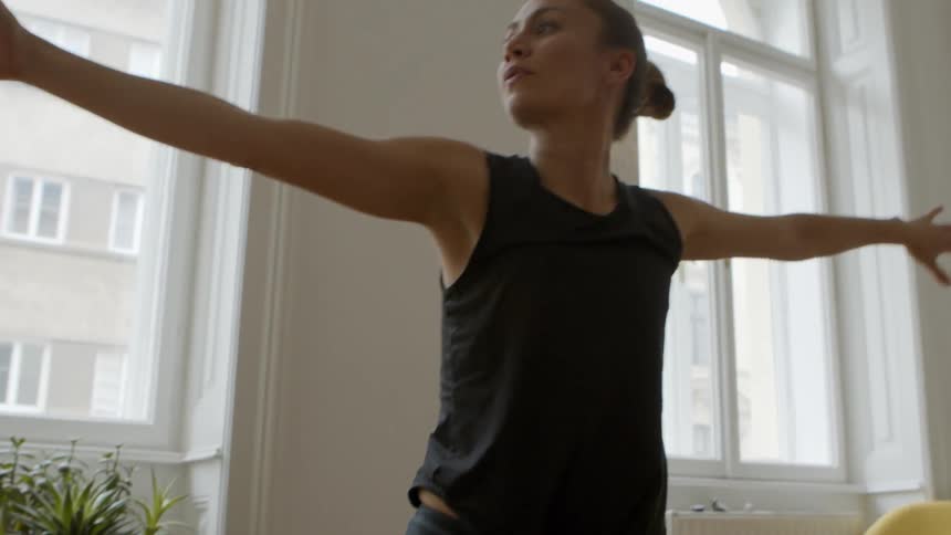 A woman stands on a yoga mat and stretches up