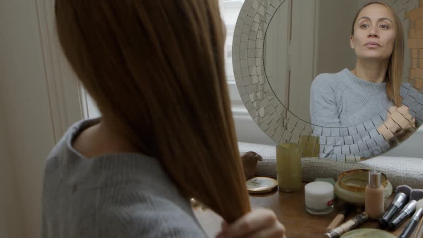A woman combs her hair while looking in a mirror