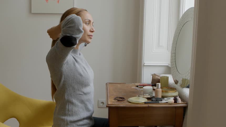A woman tying her hair while sitting at a vanity