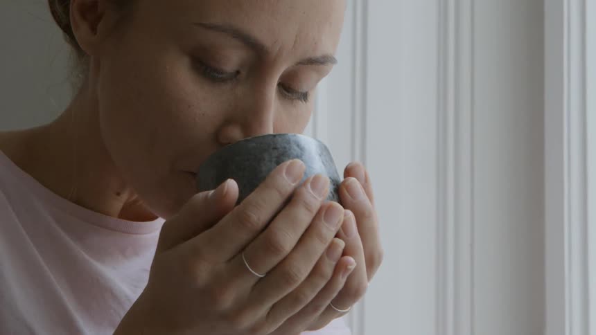 A woman raises a mug and takes a drink