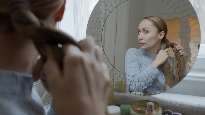 Woman braiding her hair standing in front of mirror