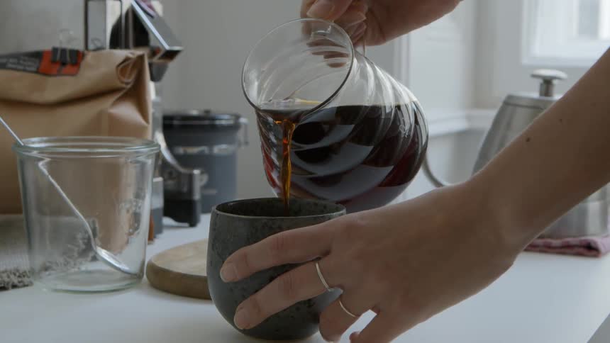 Close up of hands pouring home brewed tea into a mug