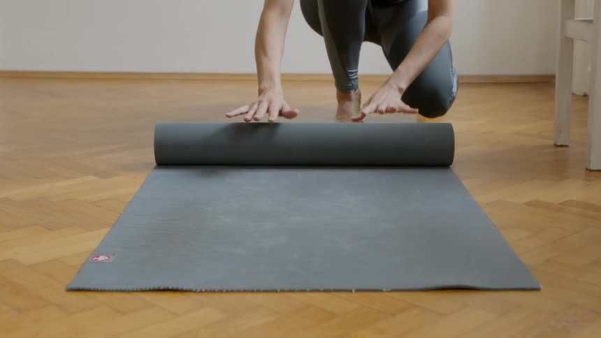 Woman rolls up yoga mat on hardwood floor