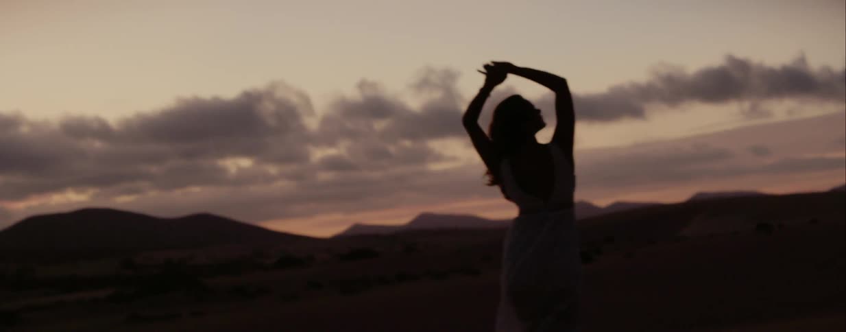 Woman stretches as she stands in a field at dawn