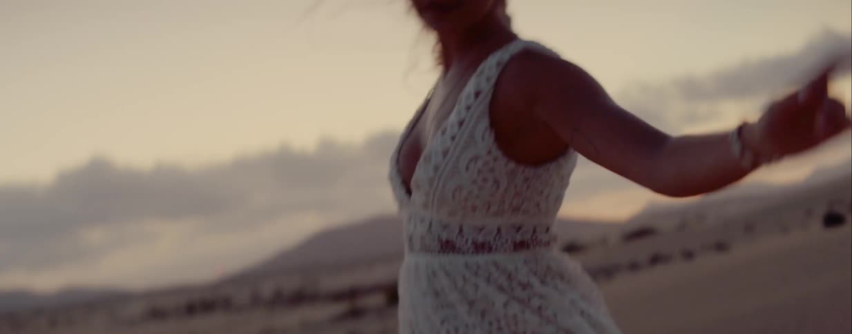 A female wearing a lace dress twirls and dances in the sand of the desert