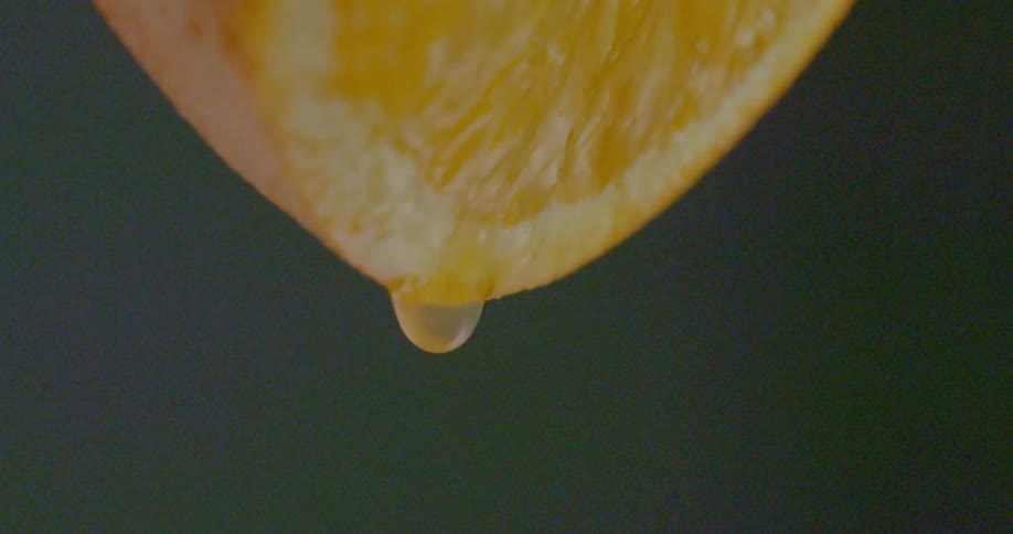 A droplet of juice drips from an orange
