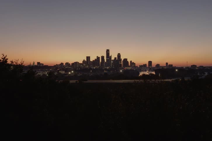A dusk to dawn time lapse of highway traffic with a citys skyline in the background