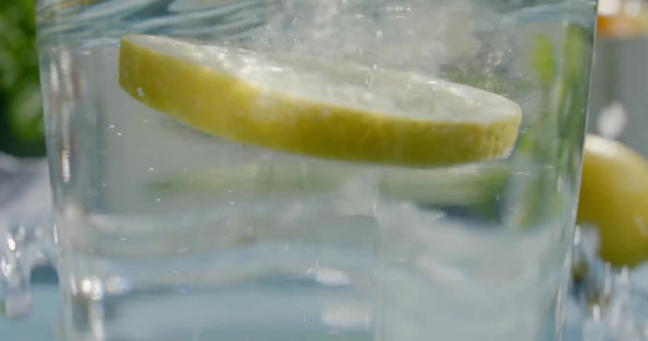 A lemon slice is dropped into the water splashing it everywhere