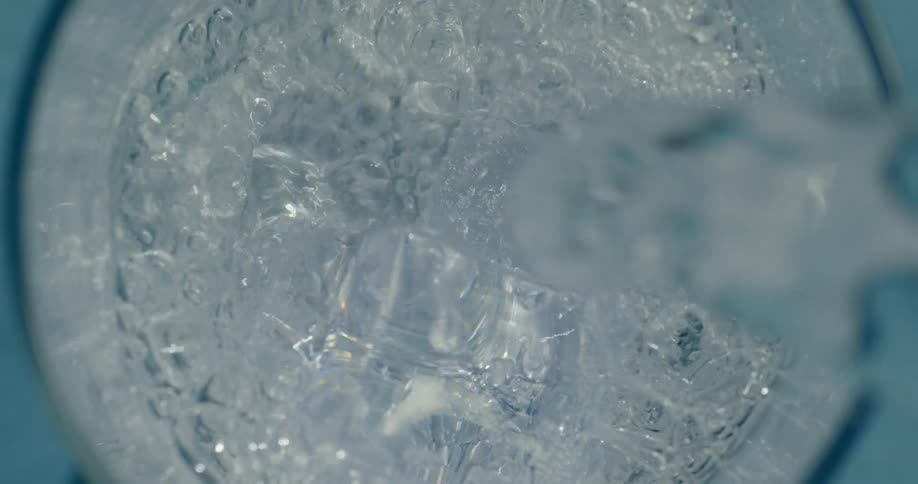 Water is poured and splashes down on ice cubes in a glass