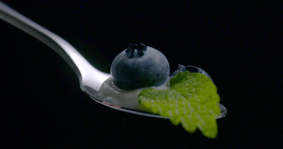 A blueberry on a spoon sits in cream with a mint leaf