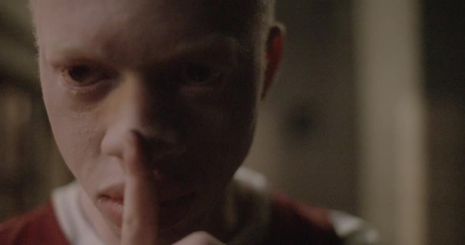A male teenager puts his finger over his lips as if telling someone to be quiet