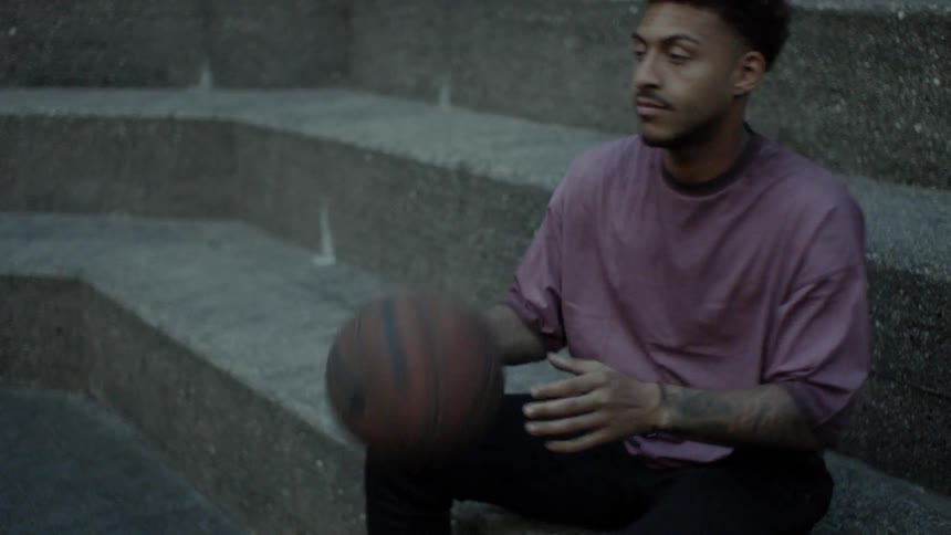 Young black man sitting on concrete steps catches and tosses basketball