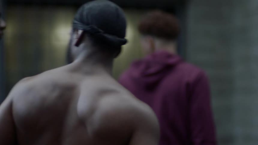 A shirtless and muscular male walks with two other young males outside of a building