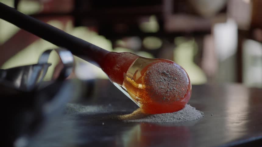 Glass maker coats glass globe in powder on metal surface