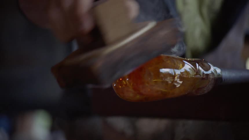 Man works with hot molten glass on a metal rod