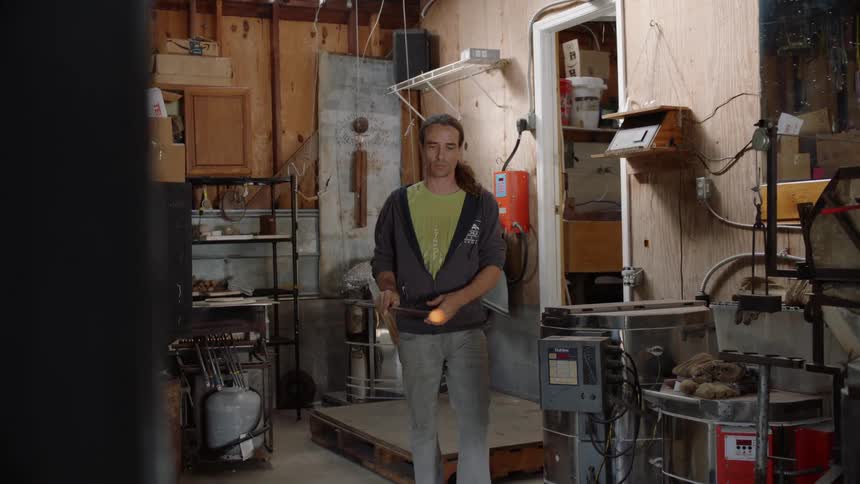 A glass blower carries a tool with hot glass in a workshop