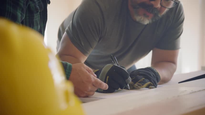 Two men talk while looking at blueprints