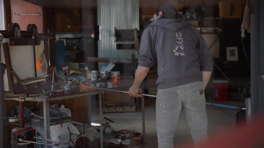 A man is forming glass in a workshop outside