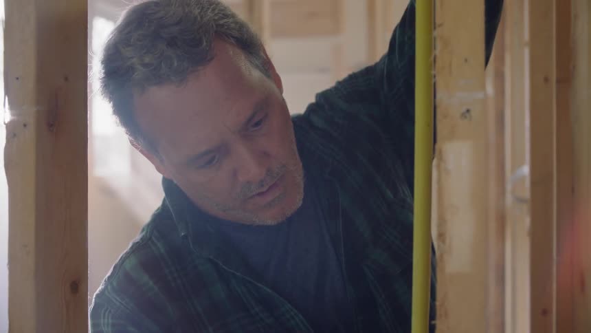 A carpenter uses a measuring tape to help mark a piece of wood