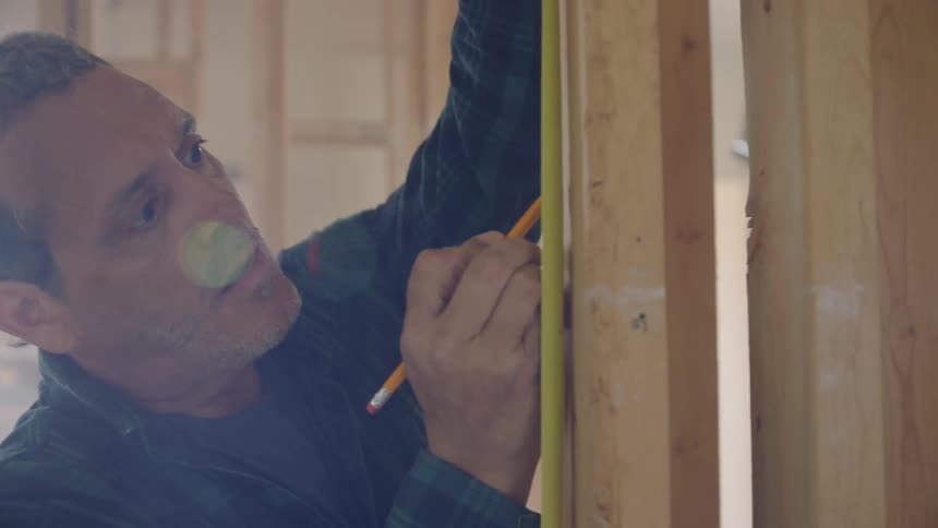 Man uses a pencil and measuring tape to place marks on the wooden frame