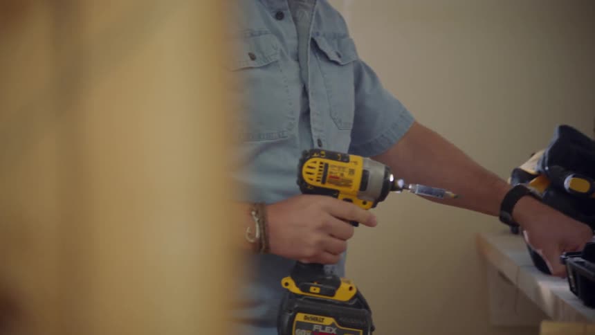 Man picks up a drill and some bits from a work table