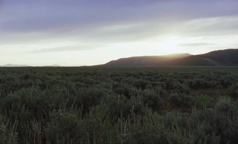 Sun rises behind mountains on horizon near plain