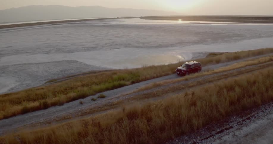 A vehicle drives along a road beside the water