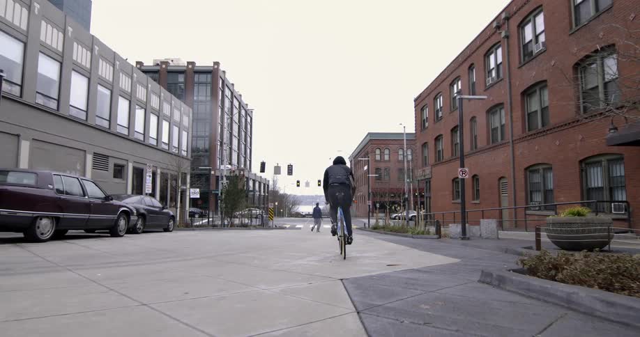 Slow-motion clip of a man on a racing bicycle riding on the sidewalk area near a city street
