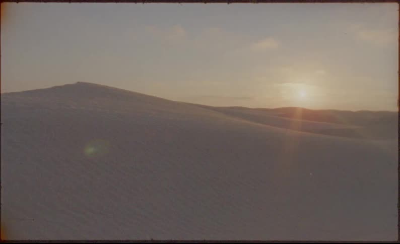 A sandy desert with the sun and the sky in the background