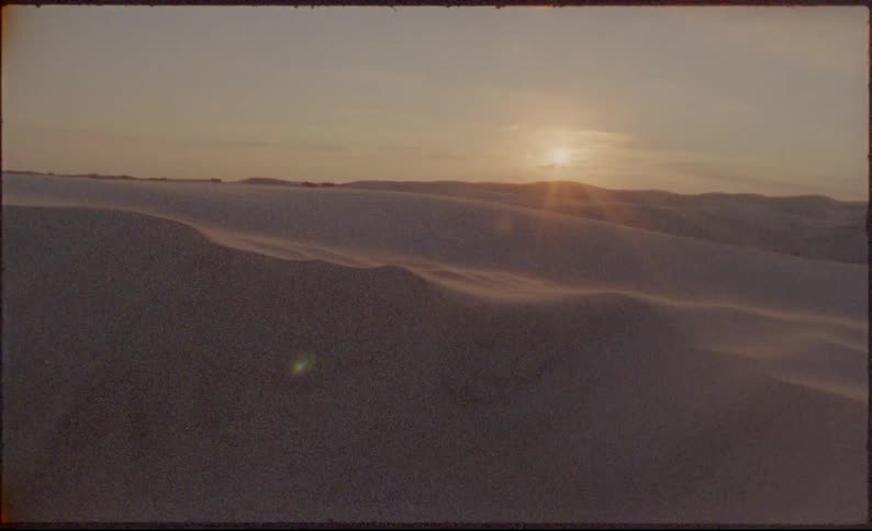 Sun hovers on horizon near hills lighting sand dunes