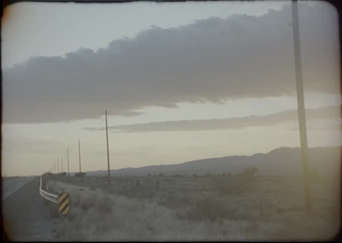 Vintage footage of a electric pole near rural road on plains at sunset