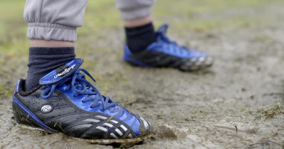 Small feet in baseball cleats take a stance in the muddy dirt