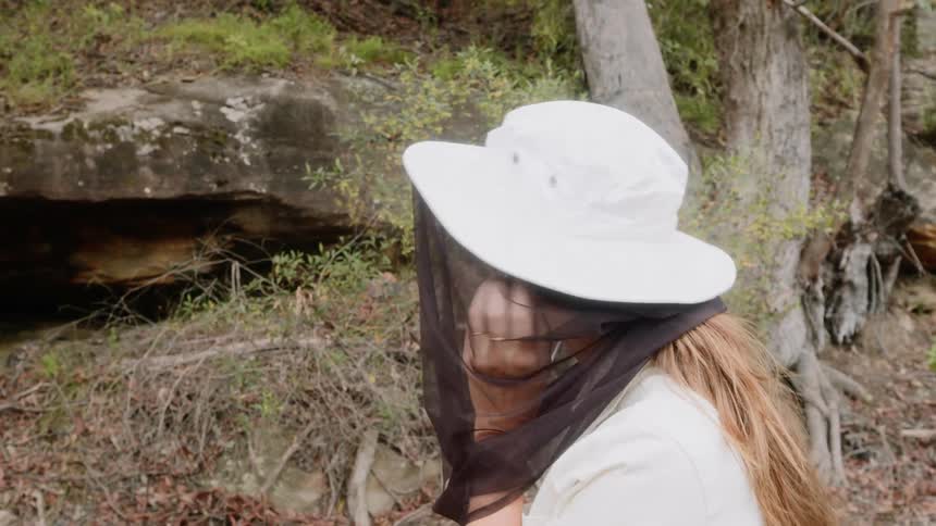 A woman puts on a safari hat with long black netting and adjusts it