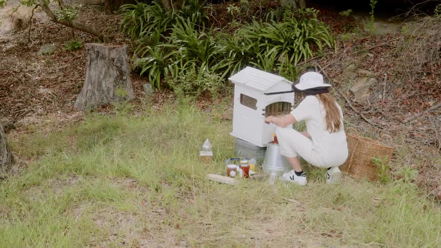 Beekeeper crouches near beehive filling jars with jelly
