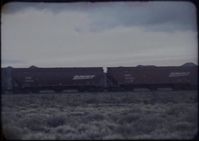 Train travels down the tracks near a field under a cloudy sky