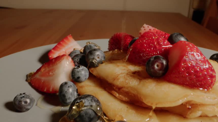 Syrup is poured on a plate of pancakes