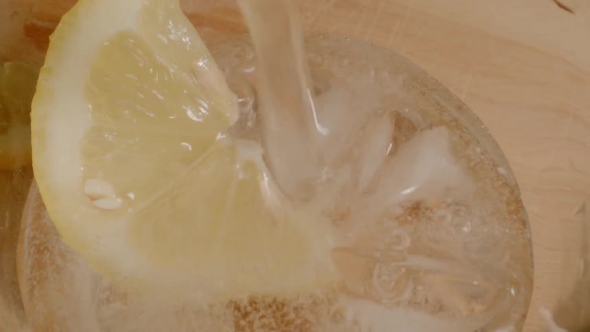 A beverage is being poured in a glass with a lemon in it
