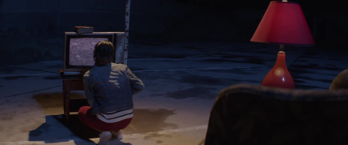 A woman turns on the tv in the parking lot and sits down