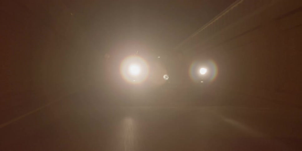 A vehicle traveling across a bridge and down a slope during the night